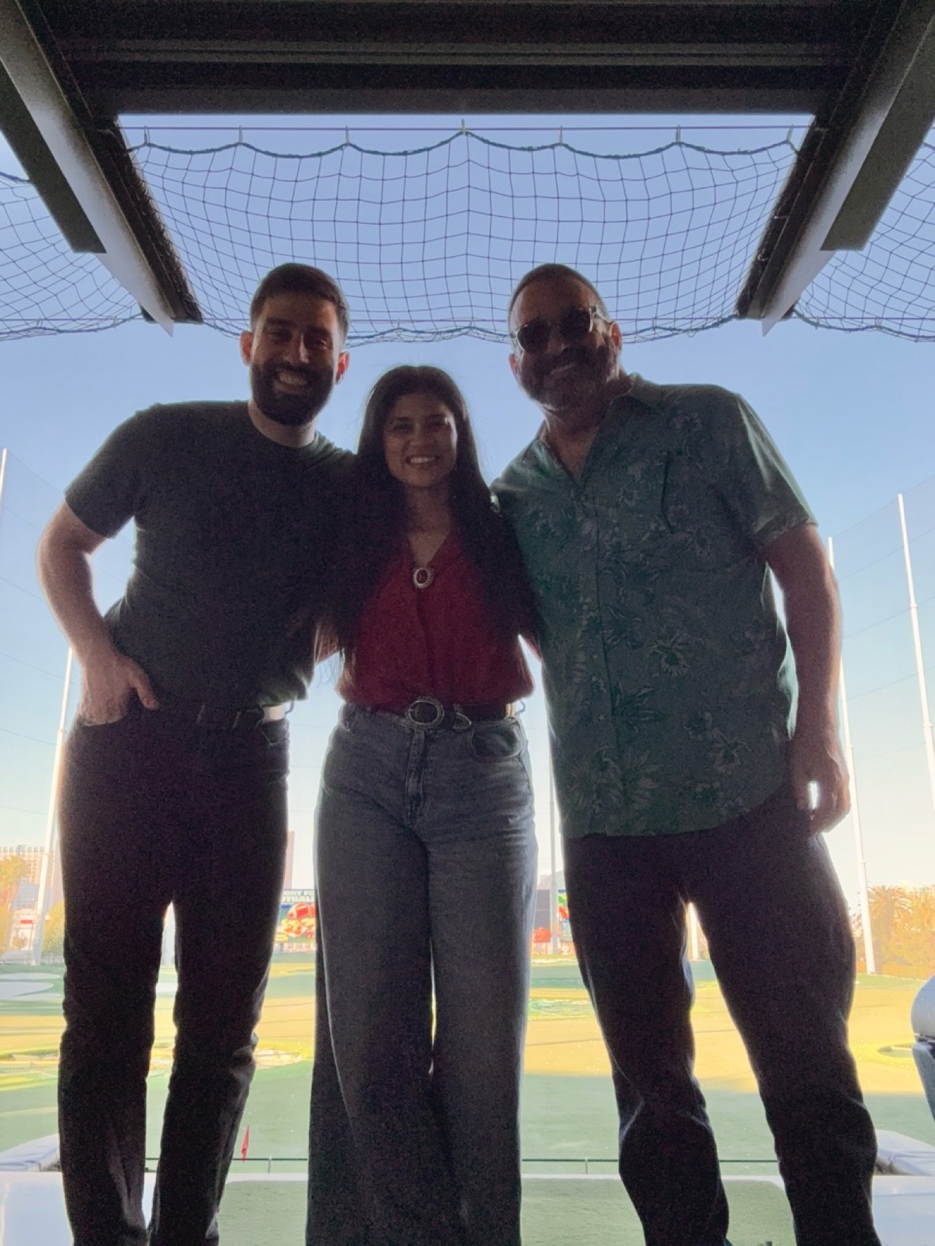 Adam, his fiancée, and Alan smiling together at Topgolf